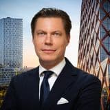 En man i kostym framför två skyskrapor i glas